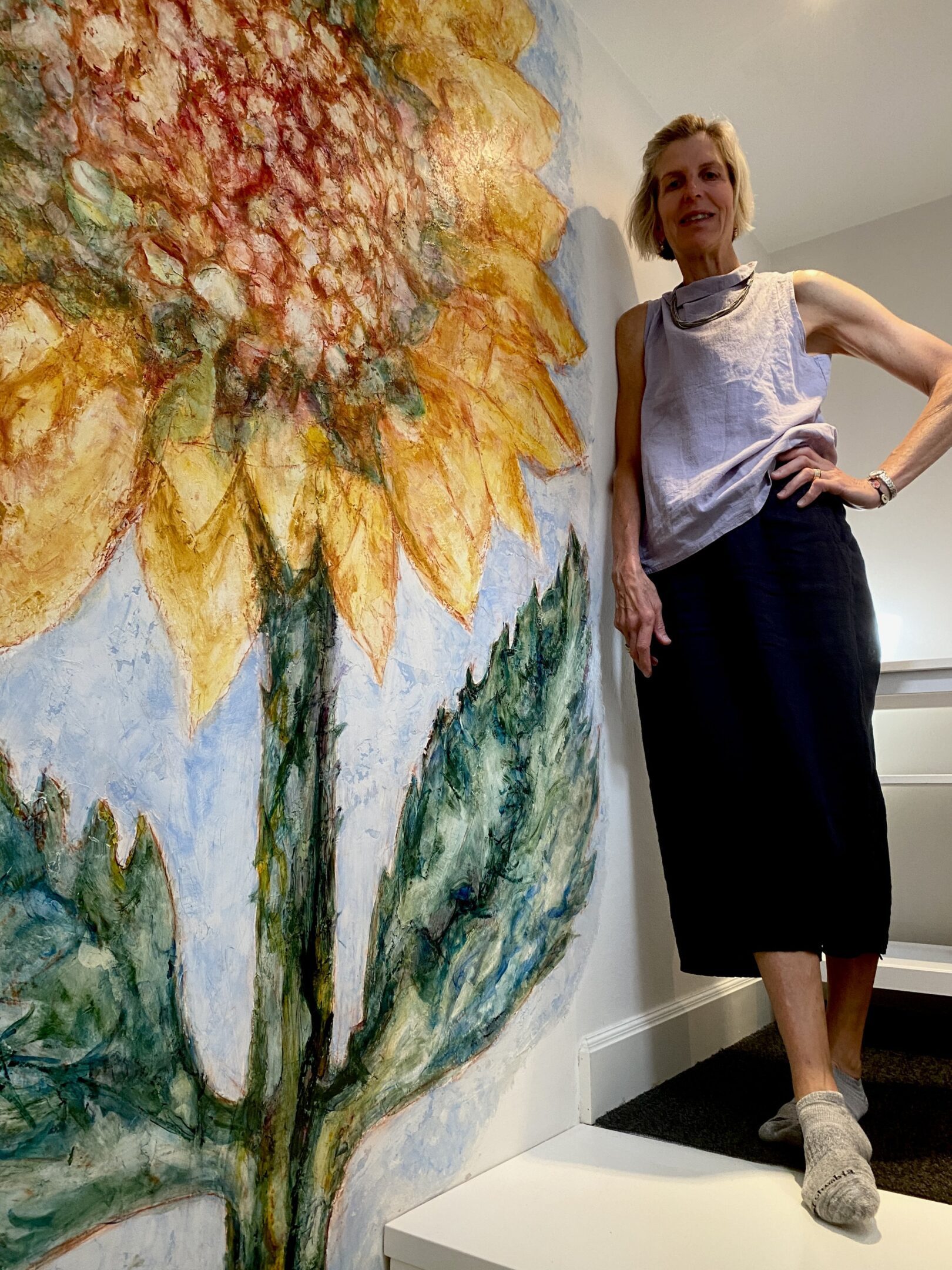 Woman standing beside large sunflower painting.